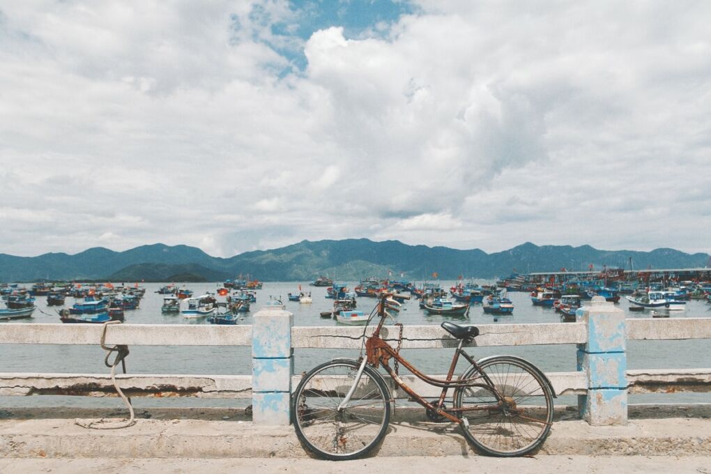 Fishing boats in the sea behind a bicycle against a fence in Nha Trang Vietnam