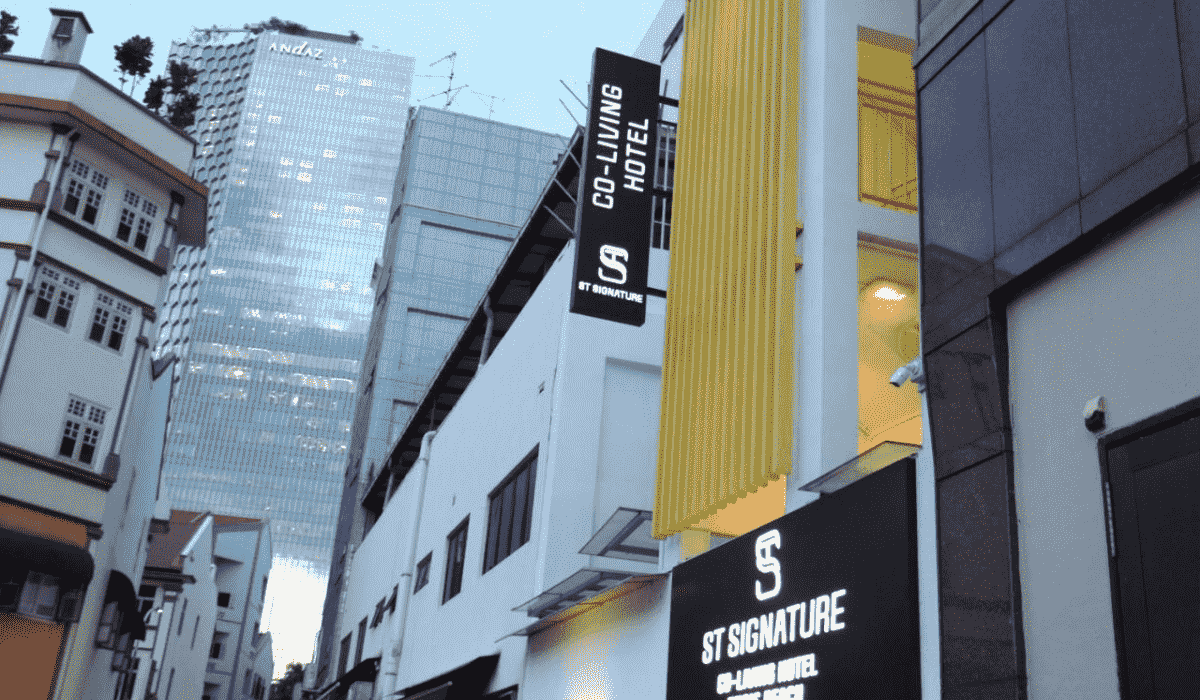 A building in Singapore with a black and white sign reading " ST Singnature, Co-living Hotel."