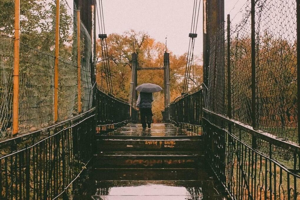 Person walking in the rain on a bridge in Taraz