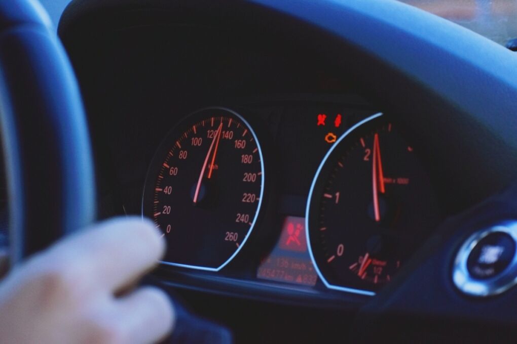 A closeup of a car's speedometer showing a high speed while someone is driving