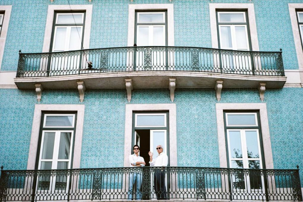 Two men standing on the balcony of a blue tiled building 
