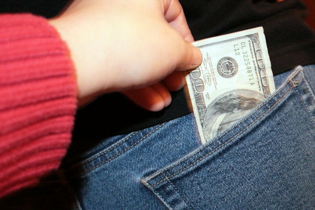 Person's hand reaching to take money out of the back pocket of someone's pants
