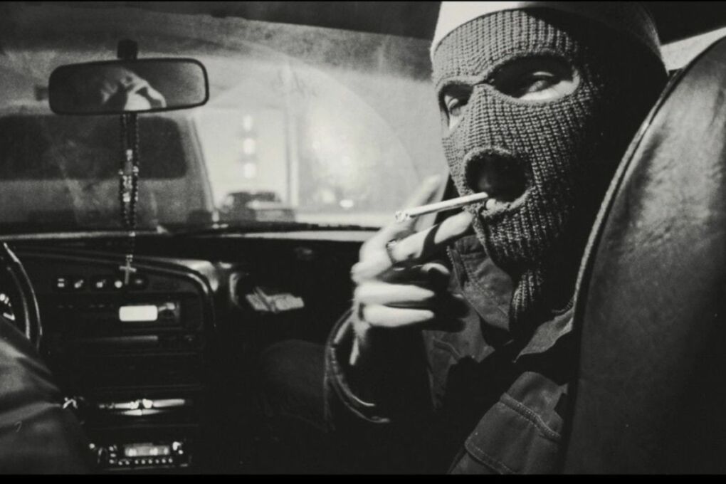 Person sitting in a car, wearing a ski mask while smoking.