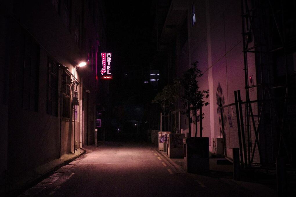A dimly lit alleyway with a lit up vacancy motel sign in it.