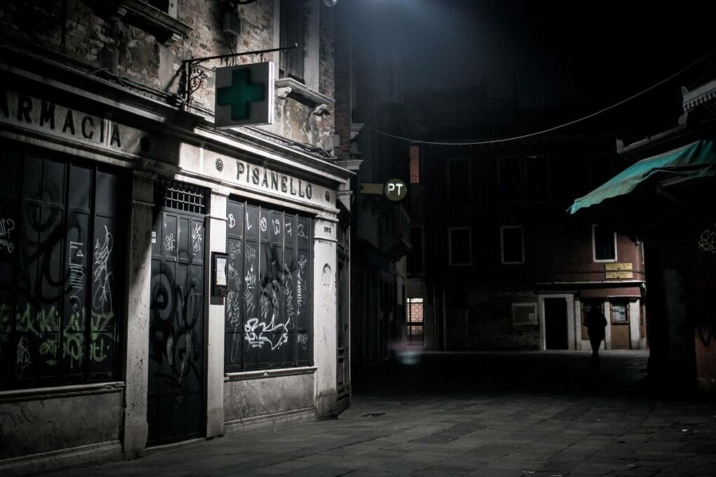 A dark street with only one light and a building covered in graffiti.