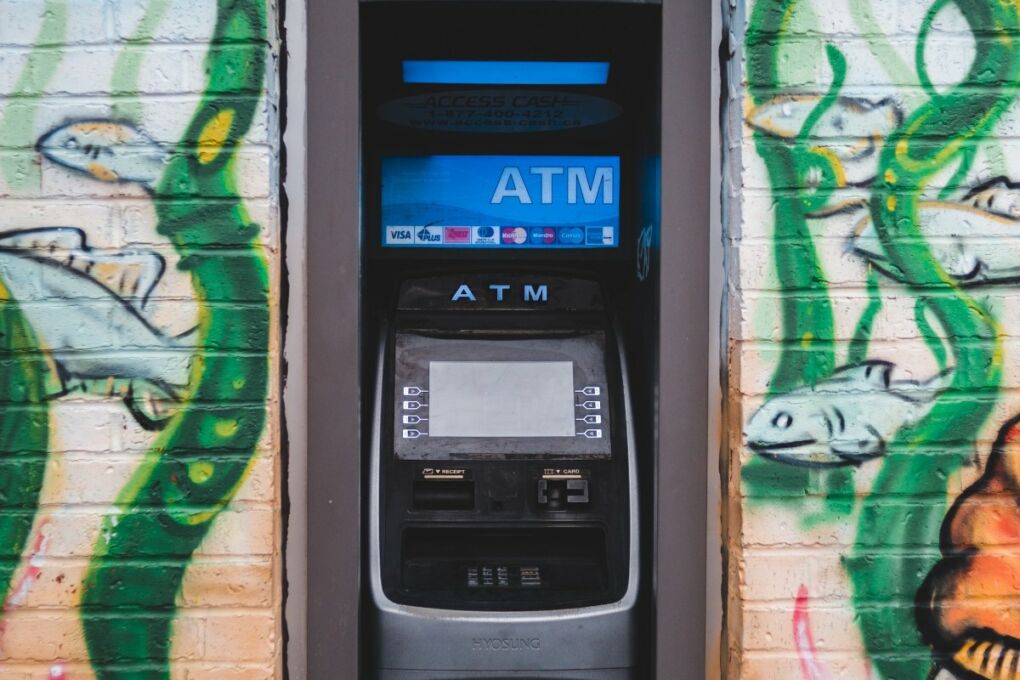 An ATM machine in the middle of a wall covered in graffiti 