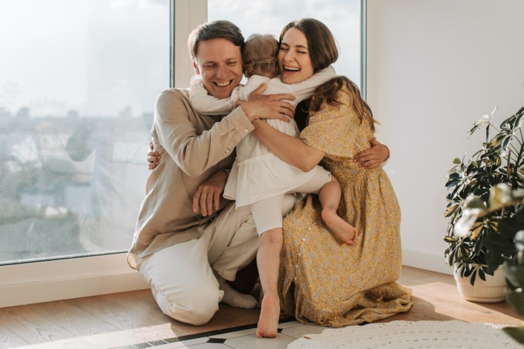 A smiling family (2 parents and one young child) embracing each other