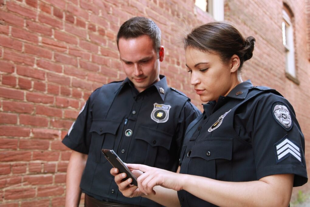 Two police officers in uniform looking serious while checking a cellphone 