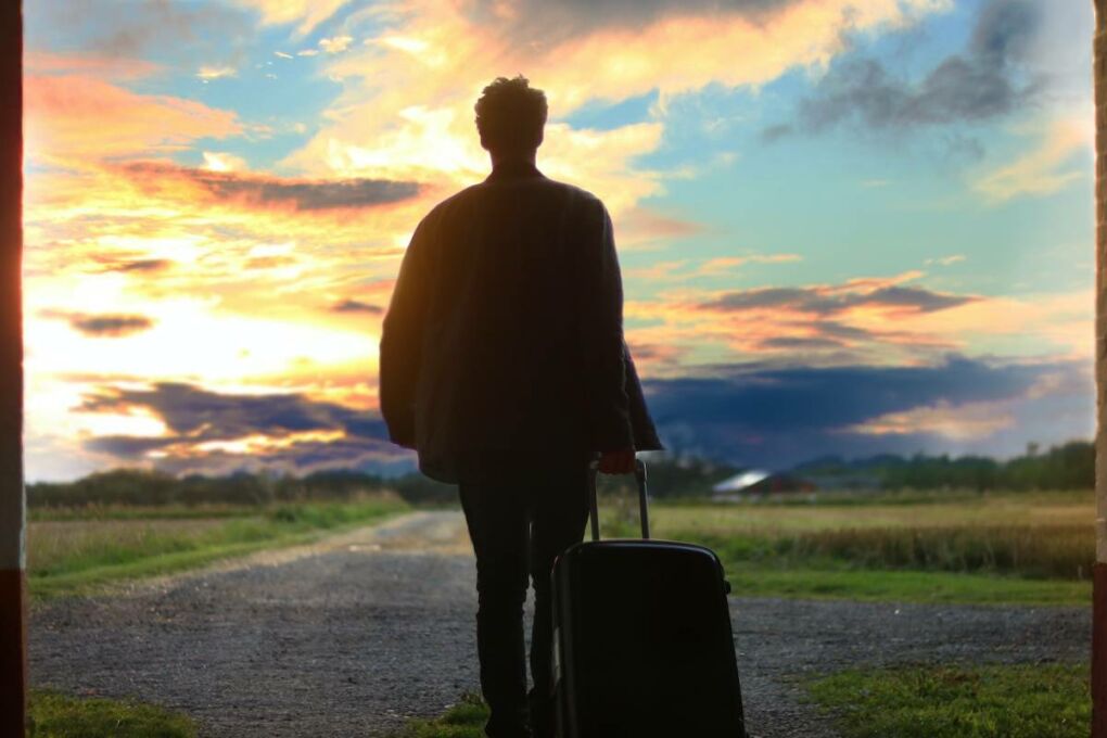 A man travelling witch a luggage bag behind him, with a sunset backdrop.