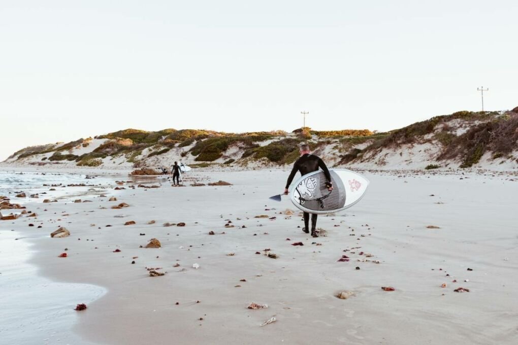 A surfer walking along a beach in Port Elizabeth, South Africa.