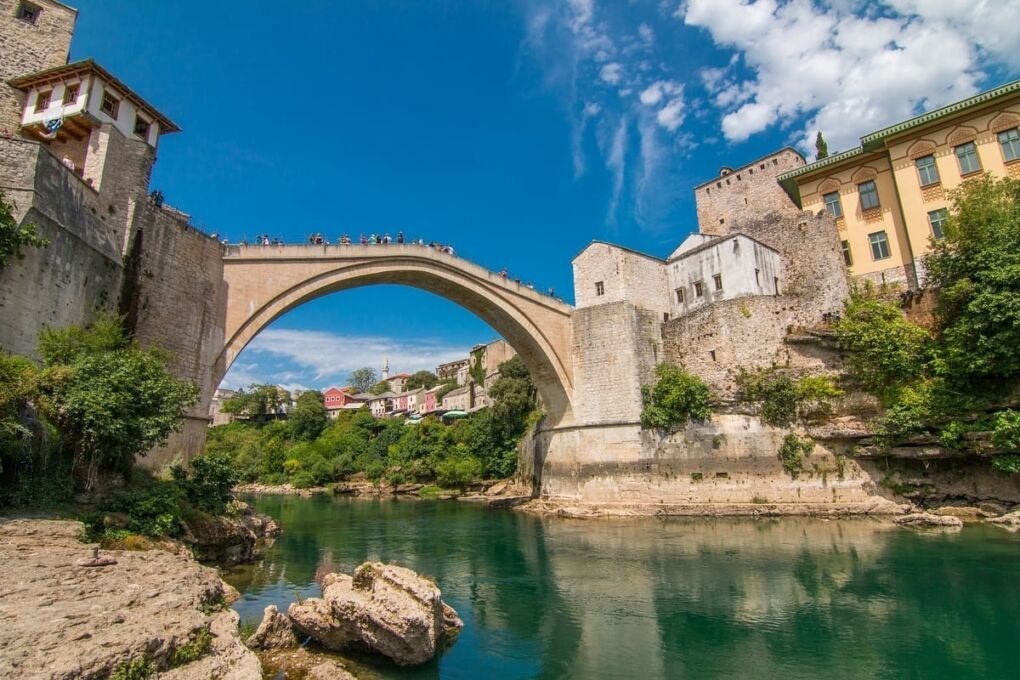 bridge spanning a river|dark brown building with blue roof|sofia cathedral landscsape|aerial view of lake with town around it|city buildings in istanbul|modern bridge in serbia|ancient greek ruins in athens|beautifully designed building|view from mountain overlooking split croatia|market stalls in bosnia|river canal in slovenia