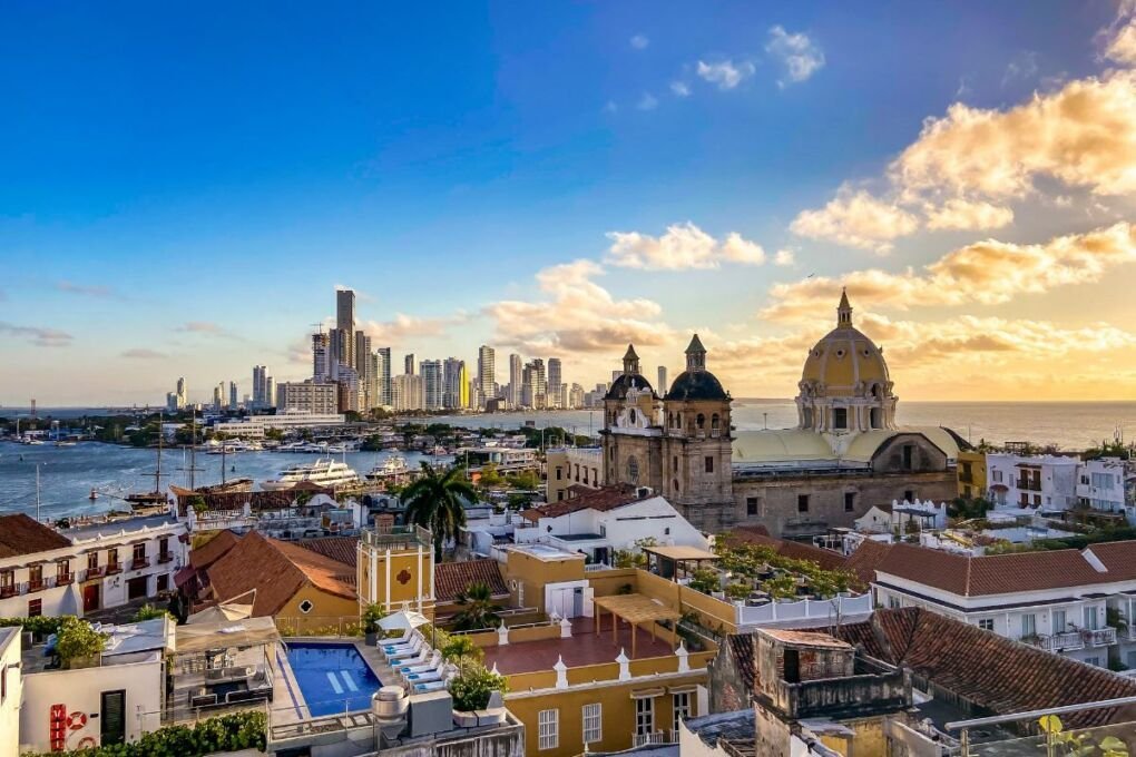 A beautiful city view of Cartagena Colombia|A street art market in Cartagena|Umbrella tourist attraction in Cartagena|A busy beach in Cartagena Colombia|A fruit seller in traditional dress in Colombia|Cartegena Old Town skyline|The colorful streets of Cartagena Old Town|Cartagena skyline at night|Street art in Cartagena|A dangerous impoverished area in Cartagena