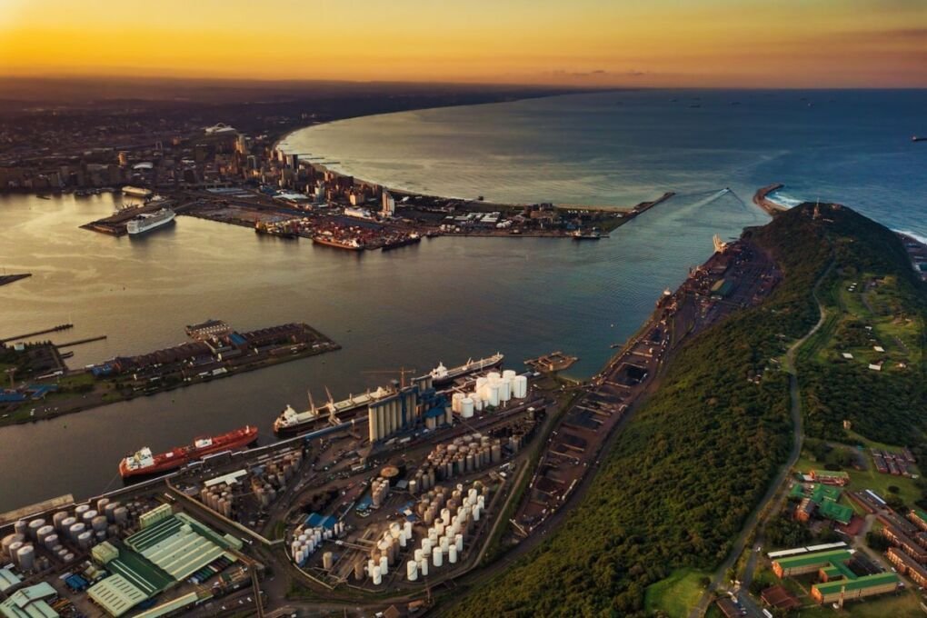 An aerial view of coastal Durban at sunset|An ATM machine in the middle of a wall covered in graffiti|Cityscape showing lots of buildings in Durban|A shark swimming in an aquarium tank at uShaka Marine World|A smiling family (2 parents and one young child) embracing each other|A reception sign on a hotel front desk|People relaxing on the beach and swimming in the ocean|Closeup of a person drinking a clear glass of water|A person putting cash into a cup held by a beggar who is also holding a sign saying "help"|Two police officers in uniform looking serious while checking a cellphone|Closeup of a water lily on the surface of a pond