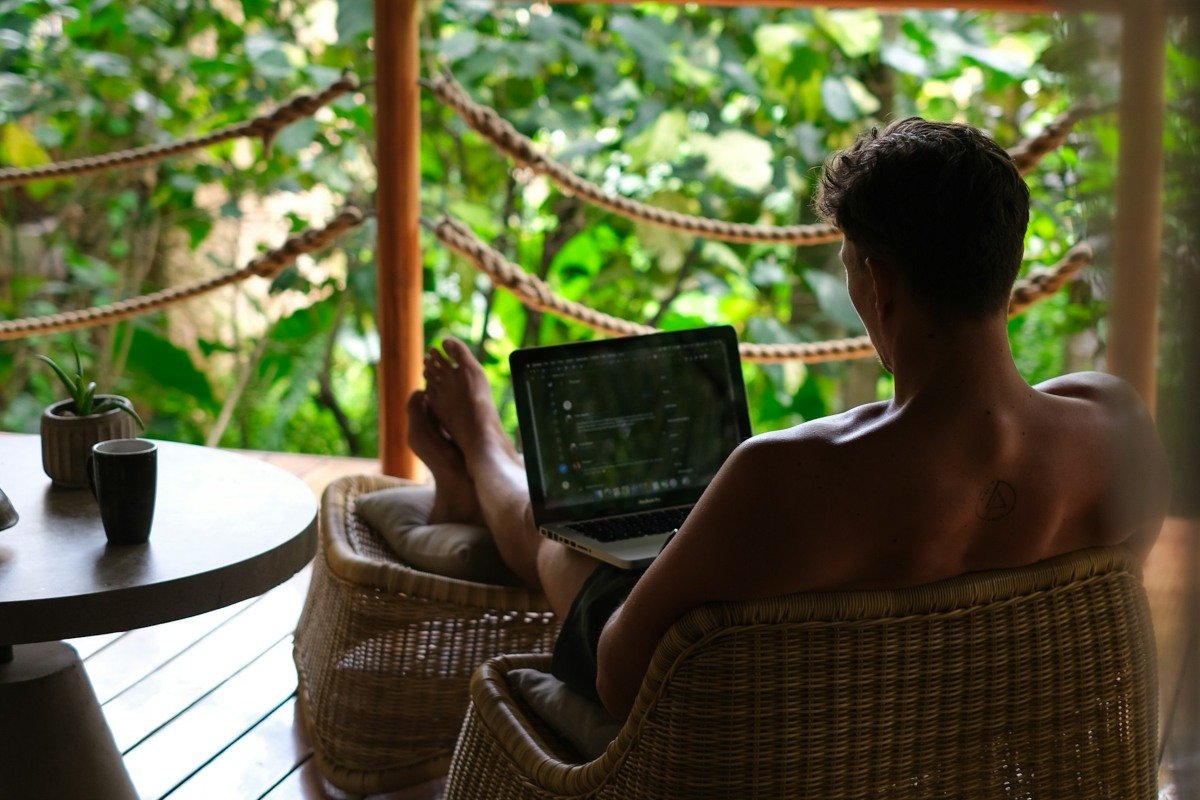 Man working remotely outside with a laptop on his lap